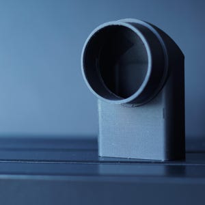 May include: A gray, right-angled pipe fitting with a circular opening. The fitting is made of a solid, matte material and is set against a gradient blue background. The design suggests a plumbing or industrial component.