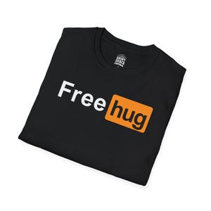 Puede incluir: Camiseta negra con las palabras "Free hug" en blanco y naranja. La palabra "Free" está en una fuente grande y en negrita, y "hug" está en un cuadro naranja más pequeño. La camiseta está doblada.