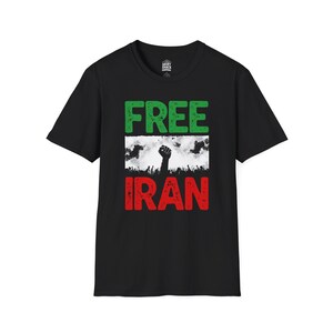 Pode incluir: Camiseta preta com as palavras "FREE IRAN" em letras de bloco verdes e vermelhas. A palavra "FREE" está acima de um gráfico de um punho erguido e uma multidão de pessoas. A camiseta é de gola redonda.