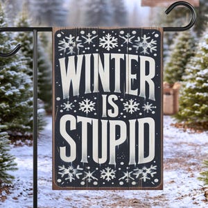 May include: A rectangular garden flag with a dark wood-grain background featuring the white text WINTER IS STUPID in a bold, stylized font. The design is decorated with various white snowflake patterns and small dots, creating a winter-themed aesthetic.