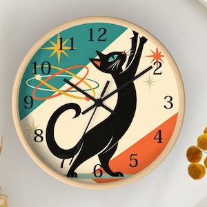 May include: A round wall clock with a light wood frame. The clock face features a black cat with raised arms, set against a retro design with teal, orange, and cream colors. The clock hands are black.