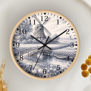 May include: Round wall clock with a light wood frame. The clock face features a black and white landscape scene with a windmill, bridge, and boat. Black hands indicate the time. Numbers are in black.