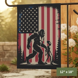 May include: A garden flag with a distressed American flag design. A black silhouette of Bigfoot walks with an alien. The flag measures 30.5cm x 45.7cm.