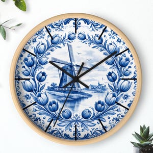 Könnte beinhalten: Runde Wanduhr mit hellem Holzrahmen. Das Zifferblatt zeigt eine blau-weiße holländische Windmühle, umgeben von einem floralen Rand. Schwarze Zeiger und Stundenmarkierungen.