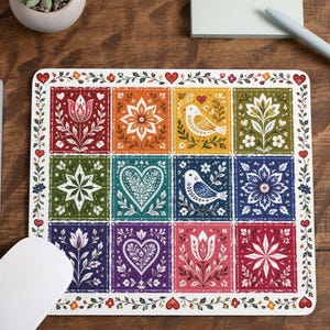 May include: A rectangular mouse pad featuring a grid of twelve colorful squares, each decorated with folk-art style illustrations of flowers, birds, and hearts in shades of red, orange, yellow, green, blue, and purple, framed by a floral border.