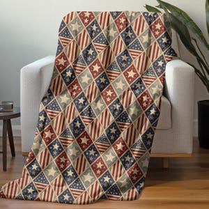 May include: A patterned throw blanket in red, white, and blue, draped over a white armchair. The blanket's design features diamond shapes with stars and stripes, reminiscent of the American flag. The blanket is made of a soft material.