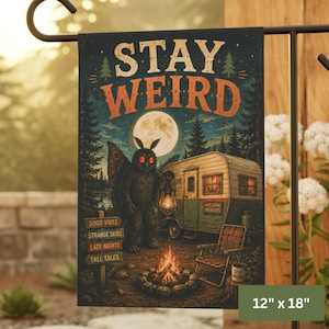 May include: A decorative garden flag with the text "STAY WEIRD" above an illustration of a mothman, a camper, and a campfire. The flag measures 12 inches by 18 inches.