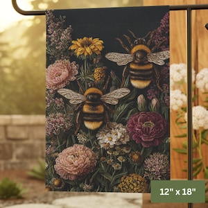May include: A garden flag featuring a detailed illustration of two bumblebees amidst a variety of flowers. The flag is 12 inches by 18 inches and showcases a dark background with pink, yellow, and purple floral elements.