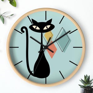 May include: A round wall clock with a light wood frame. The clock face is light blue with a black cat illustration and three diamond shapes in yellow, orange, and blue. Black clock hands and black lines mark the hours.