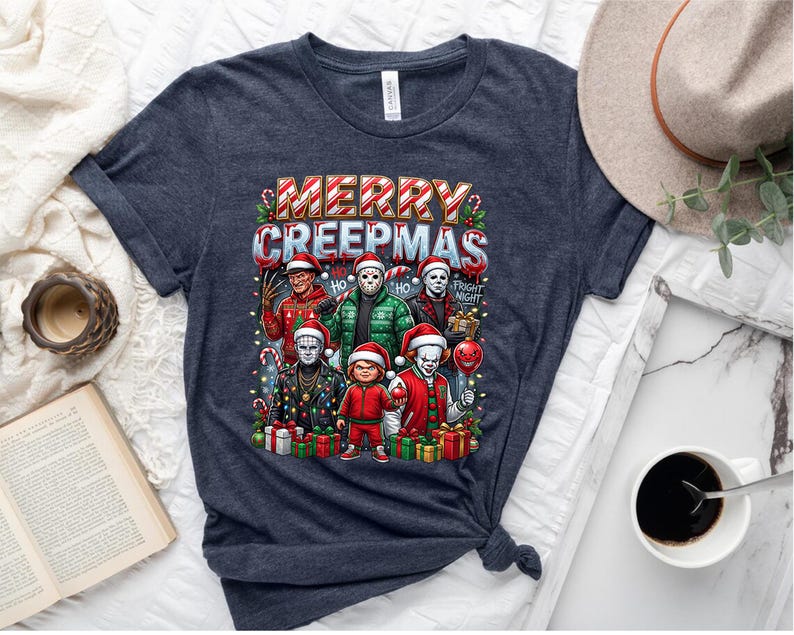 Puede incluir: Camiseta azul oscuro con el texto "MERRY CREEPMAS" e ilustraciones de personajes de pel&iacute;culas de terror con gorros de Pap&aacute; Noel. El dise&ntilde;o incluye bastones de caramelo, luces navide&ntilde;as y regalos. La camiseta es de un material suave.