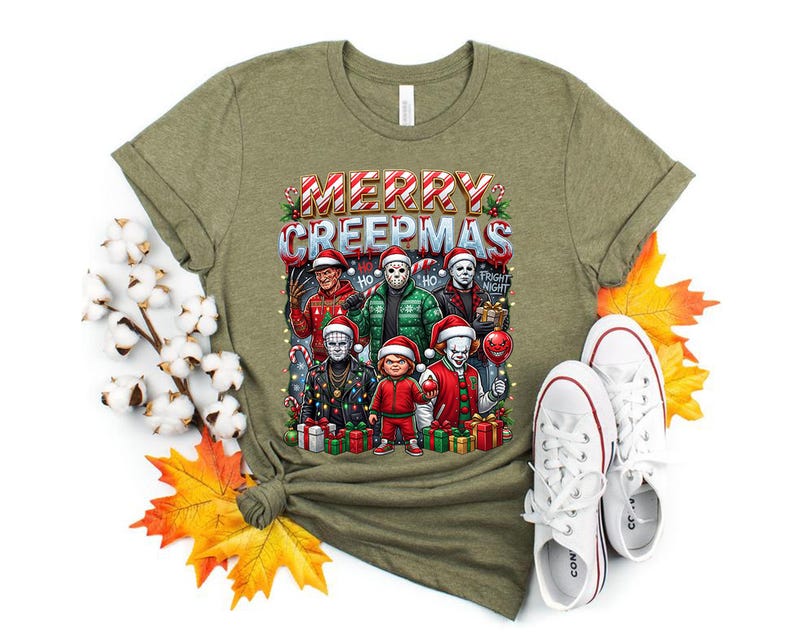Puede incluir: Camiseta verde oliva con un gr&aacute;fico festivo de personajes de pel&iacute;culas de terror con gorros de Pap&aacute; Noel y el texto "MERRY CREEPMAS". El dise&ntilde;o incluye regalos envueltos y luces navide&ntilde;as. Zapatillas blancas junto a la camiseta.