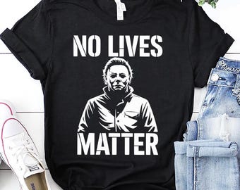 May include: Black t-shirt featuring the text "NO LIVES MATTER" in white above a white graphic of a person's face. The word "MATTER" is printed in white below the graphic. White trainers and blue jeans are visible in the background.