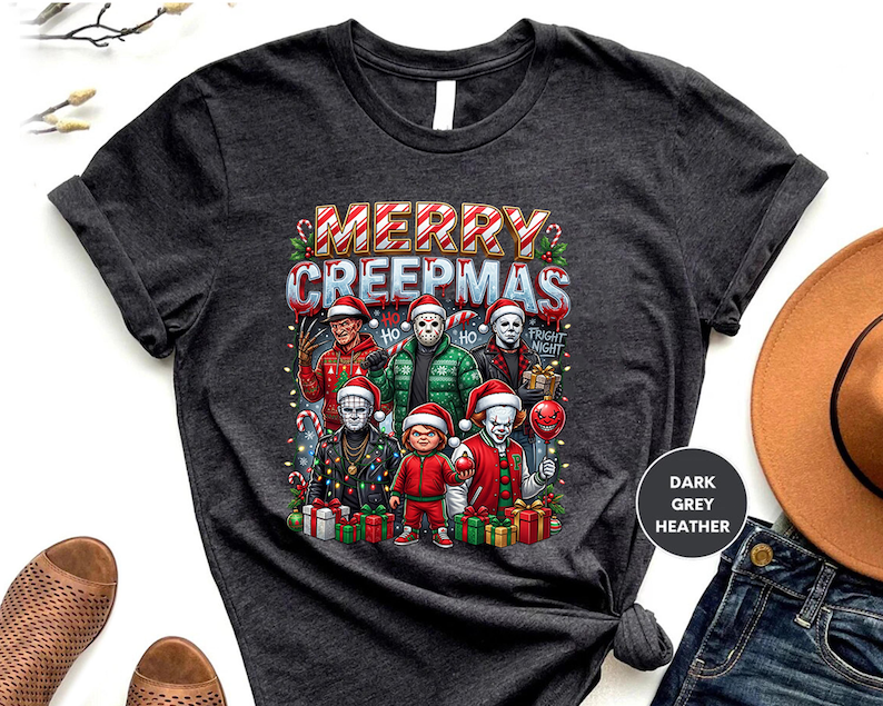 Puede incluir: Camiseta gris oscuro jaspeado con el texto "MERRY CREEPMAS" e im&aacute;genes de personajes de pel&iacute;culas de terror con gorros de Pap&aacute; Noel. El dise&ntilde;o incluye bastones de caramelo, luces navide&ntilde;as y cajas de regalo. La camiseta es de cuello redondo.