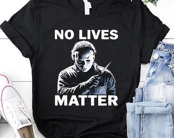 May include: Black t-shirt featuring the text "NO LIVES MATTER" and an illustration of a masked figure holding a knife. The figure is in monochrome, with a sinister look. The t-shirt is displayed on a white surface.