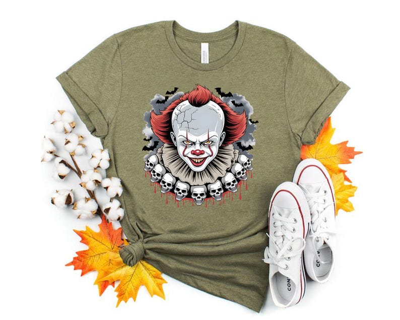 Puede incluir: Camiseta verde oliva con un gr&aacute;fico de payaso aterrador. El payaso tiene pelo rojo, cara blanca y un cuello con volantes adornado con calaveras. El dise&ntilde;o incluye murci&eacute;lagos y una cabeza agrietada. Zapatillas blancas con detalles rojos en la parte inferior.