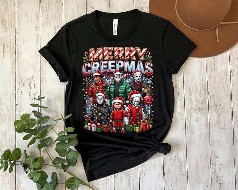 Puede incluir: Camiseta negra con la frase "MERRY CREEPMAS" y dibujos de personajes de pel&iacute;culas de terror con gorros de Pap&aacute; Noel. El dise&ntilde;o incluye luces navide&ntilde;as y regalos, creando un tema festivo y espeluznante.