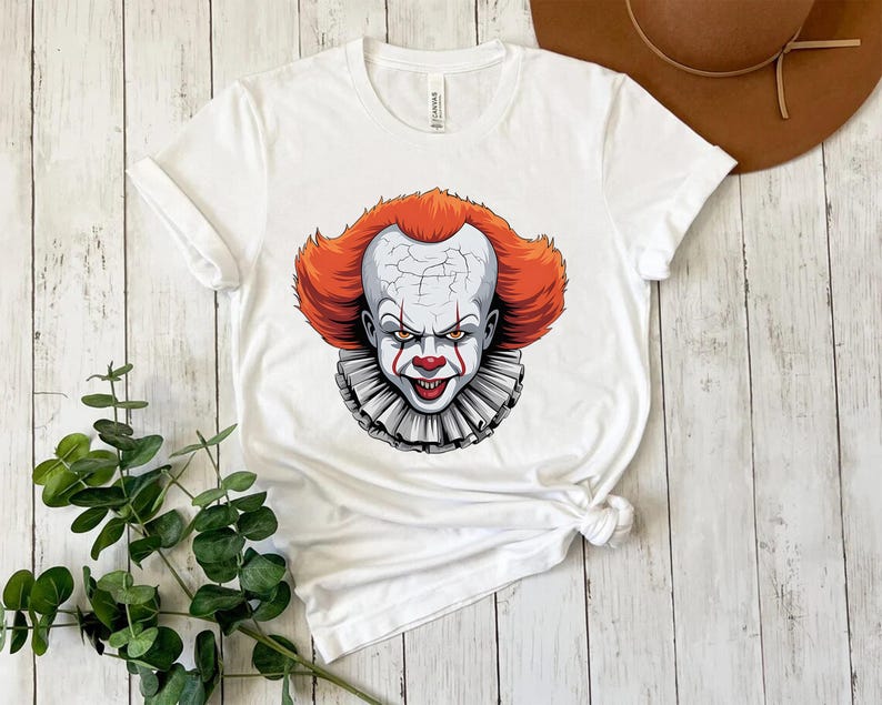 Puede incluir: Camiseta blanca con un gr&aacute;fico de un payaso aterrador con pelo rojo, cara blanca y cuello con volantes. El payaso tiene una expresi&oacute;n siniestra. La camiseta est&aacute; hecha de un material suave.