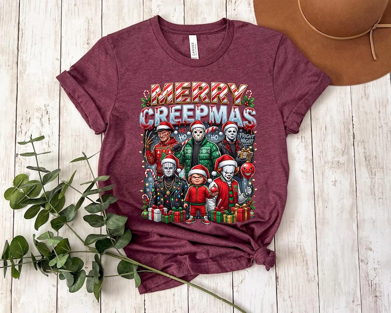 Puede incluir: Camiseta granate con el texto "MERRY CREEPMAS" sobre un gr&aacute;fico de personajes de pel&iacute;culas de terror con gorros de Pap&aacute; Noel. El gr&aacute;fico incluye personajes como Freddy Krueger y Jason Voorhees, rodeados de decoraciones navide&ntilde;as.