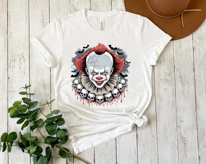 Puede incluir: Camiseta blanca con un gr&aacute;fico de un payaso aterrador con pelo rojo, cara blanca y nariz roja. El payaso est&aacute; rodeado de murci&eacute;lagos y calaveras. La camiseta es de cuello redondo y tiene mangas cortas.