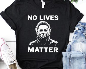 May include: Black t-shirt featuring the text "NO LIVES MATTER" above a white graphic of a man's face. The shirt is paired with white trainers and blue jeans.