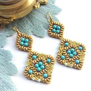 Può includere: Orecchini con perline dorate e turchesi con un design geometrico. Gli orecchini sono realizzati con piccole perline rotonde e hanno una forma quadrata pendente.