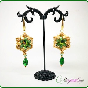 May include: Gold and green beaded earrings with a square design and a teardrop dangle. The earrings are displayed on a black stand.