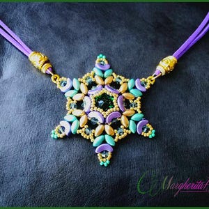 Pode incluir: Um colar com um pingente de estrela de contas douradas e roxas com uma pedra preciosa verde no centro. O colar é feito com um cordão de camurça roxo.