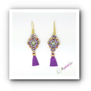 Op de afbeelding: Paarse en gouden kralen oorbellen met een kwast. De oorbellen hebben een geometrisch ontwerp in paars, goud en groen.