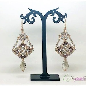 Op de afbeelding: Een paar oorhangers met een geometrisch ontwerp met een traanvormige kristal aan de onderkant. De oorbellen zijn gemaakt van zilverkleurige kralen en roze en heldere kristallen.