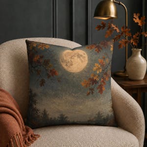 Könnte beinhalten: Ein quadratisches Zierkissen mit einem Druckmotiv, das einen Vollmond in einem nächtlichen Himmel über einem dunklen Wald zeigt. Im Vordergrund sind Zweige mit herbstlich gefärbten Eichenblättern in Orange-, Braun- und Gelbtönen zu sehen.