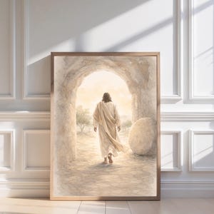 May include: A framed print shows a figure in a flowing robe walking towards a bright light. The artwork, in soft, muted tones, shows a stone archway and a large stone. The print is displayed against a white wall with molding.