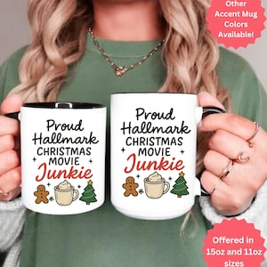 May include: Two white ceramic mugs with black handles and rims. Each mug has the text "Proud Hallmark Christmas Movie Junkie" with gingerbread man, coffee cup, and Christmas tree graphics. The mugs are available in 15oz and 11oz sizes.