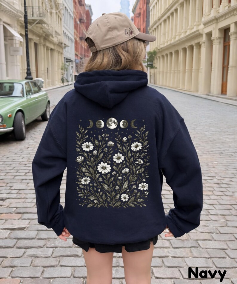 May include: Navy blue hoodie featuring a floral and moon phase design on the back. The design includes white daisies, green leaves, and a series of moon phases. The word "Navy" is printed at the bottom of the image.