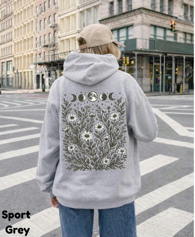 May include: Sport grey hoodie with a floral and moon phase design on the back. The design features white flowers, green leaves, and moon phases. The hoodie is a light grey color and has a hood and long sleeves. The text "Sport Grey" is at the bottom left.