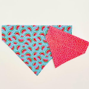 May include: Two dog bandanas. One is light blue with a watermelon pattern, featuring red watermelon slices, green rinds, and black seeds. The other is red with a white leaf pattern. Both are triangular.