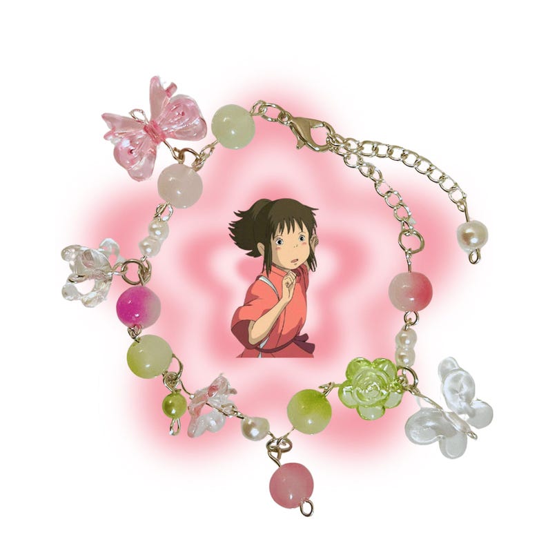 May include: A delicate bracelet featuring a variety of beads in pink, green, and white, along with clear butterfly and flower charms. The bracelet has a gold-colored chain and clasp. A cartoon image of a girl is in the background.