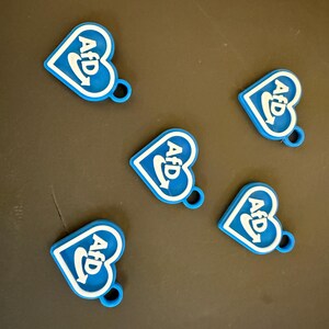 Könnte beinhalten: Fünf blaue herzförmige Anhänger mit einem weißen "AFD" Logo und einem weißen Swoosh-Design.