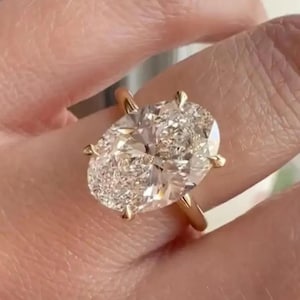 Peut inclure: Une bague en or ornée d'une grande pierre précieuse transparente taille ovale à facettes, fixée par quatre griffes. L'anneau est fin et en or poli, offrant une base simple et épurée pour cette pierre brillante qui reflète la lumière.