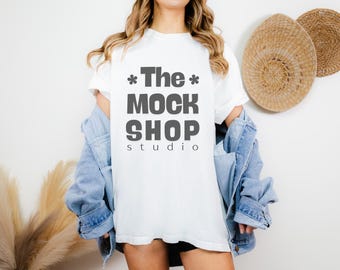 May include: A white t-shirt with the text "*The* MOCK SHOP studio" printed on the front. The shirt is being worn by a person with long brown hair and a denim jacket.
