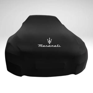 Puede incluir: Una funda de coche negra con el logotipo de Maserati en blanco. La funda está diseñada para proteger un coche de los elementos. La funda del coche está hecha de un material duradero y está diseñada para ajustarse perfectamente al coche.