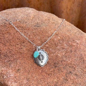 May include: A silver necklace with a turquoise pendant. The pendant is a round, scalloped design with a smaller turquoise stone hanging from it.