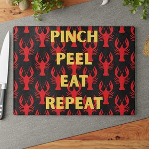 May include: A black cutting board with a red lobster pattern and the text "Pinch Peel Eat Repeat" in yellow.
