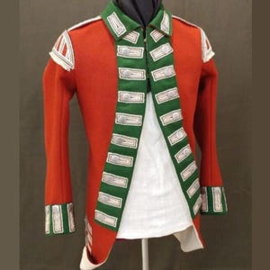 May include: A red military jacket with green and white trim. The jacket features a high collar, decorative buttons, and white accents on the shoulders and cuffs. The jacket is open, revealing a white undergarment.
