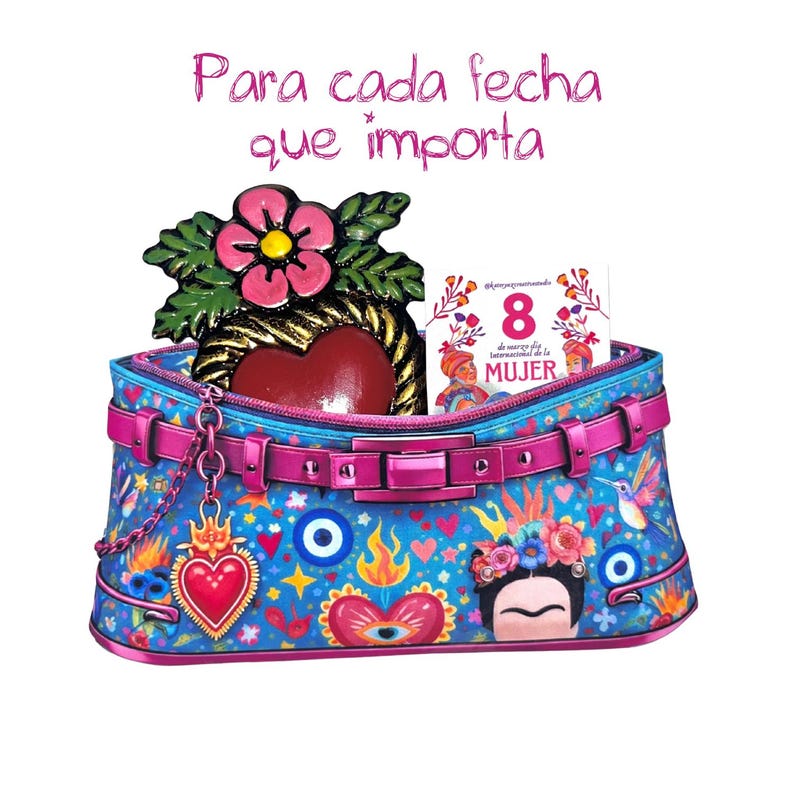 May include: A blue handbag with a pink belt and a chain, decorated with hearts, eyes, and a Frida Kahlo illustration. The bag contains a heart-shaped ornament and a card that says "8 de marzo d&iacute;a internacional de la MUJER". The text above says "Para cada fecha que importa".