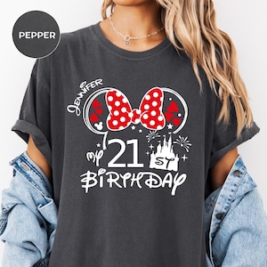 May include: Dark gray t-shirt with a Minnie Mouse-themed design. The design includes a red polka dot bow, the name "Jennifer", the number "21", the words "my birthday", and a castle graphic.