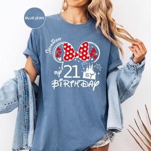 May include: Blue jean colored t-shirt with a white graphic design for a 21st birthday. The design includes a red and white polka dot bow, hearts, a castle, and the name "Jennifer".