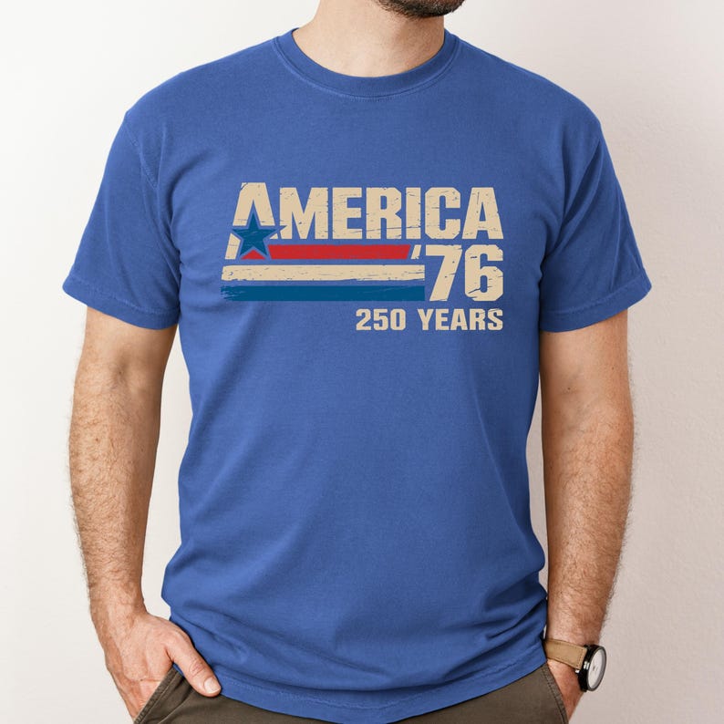 May include: Blue t-shirt featuring the text "AMERICA '76 250 YEARS" in a distressed, vintage style. The design incorporates a star and stripes in red, white, and blue, commemorating the nation's anniversary. The shirt has a crew neck.