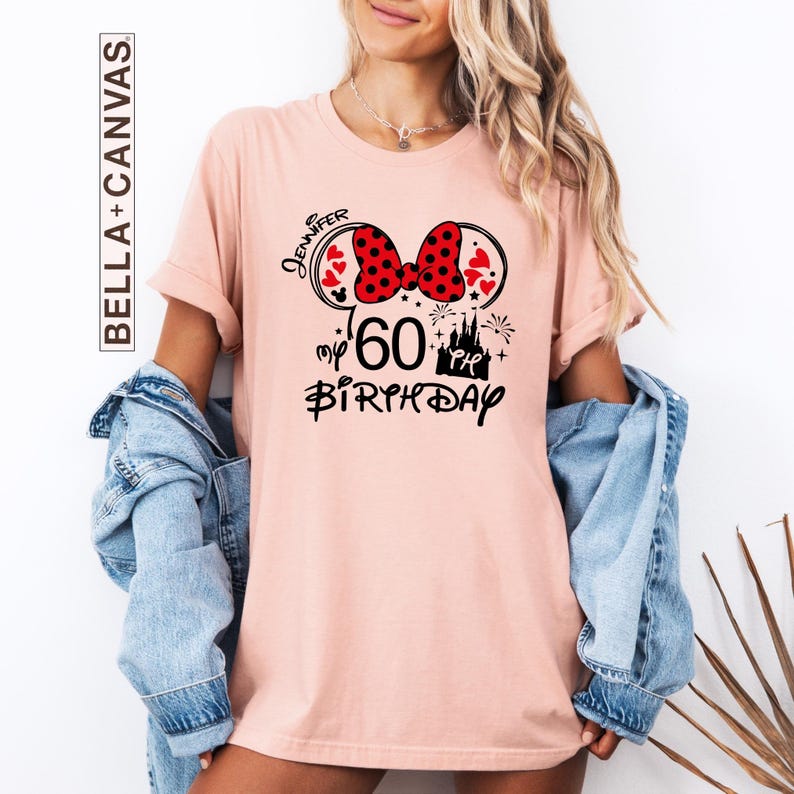 Puede incluir: Camiseta rosa claro con un dise&ntilde;o inspirado en Minnie Mouse para un 60 cumplea&ntilde;os. El dise&ntilde;o incluye un lazo rojo de lunares, orejas de rat&oacute;n, corazones, un castillo y los textos "Jennifer" y "my 60th Birthday". La camiseta es de Bella+Canvas.