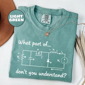 May include: Light green Comfort Colors t-shirt with the text "What part of... don't you understand?" and a circuit diagram in white. A silver necklace with a pendant is on the shirt.