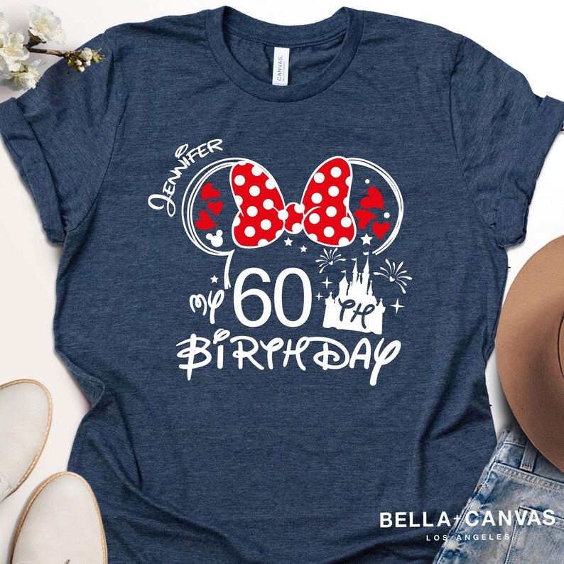 Puede incluir: Camiseta azul marino con un dise&ntilde;o gr&aacute;fico blanco. El dise&ntilde;o incluye un lazo rojo de lunares, orejas de Mickey Mouse, el nombre "Jennifer", el n&uacute;mero "60", un castillo y las palabras "my birthday".